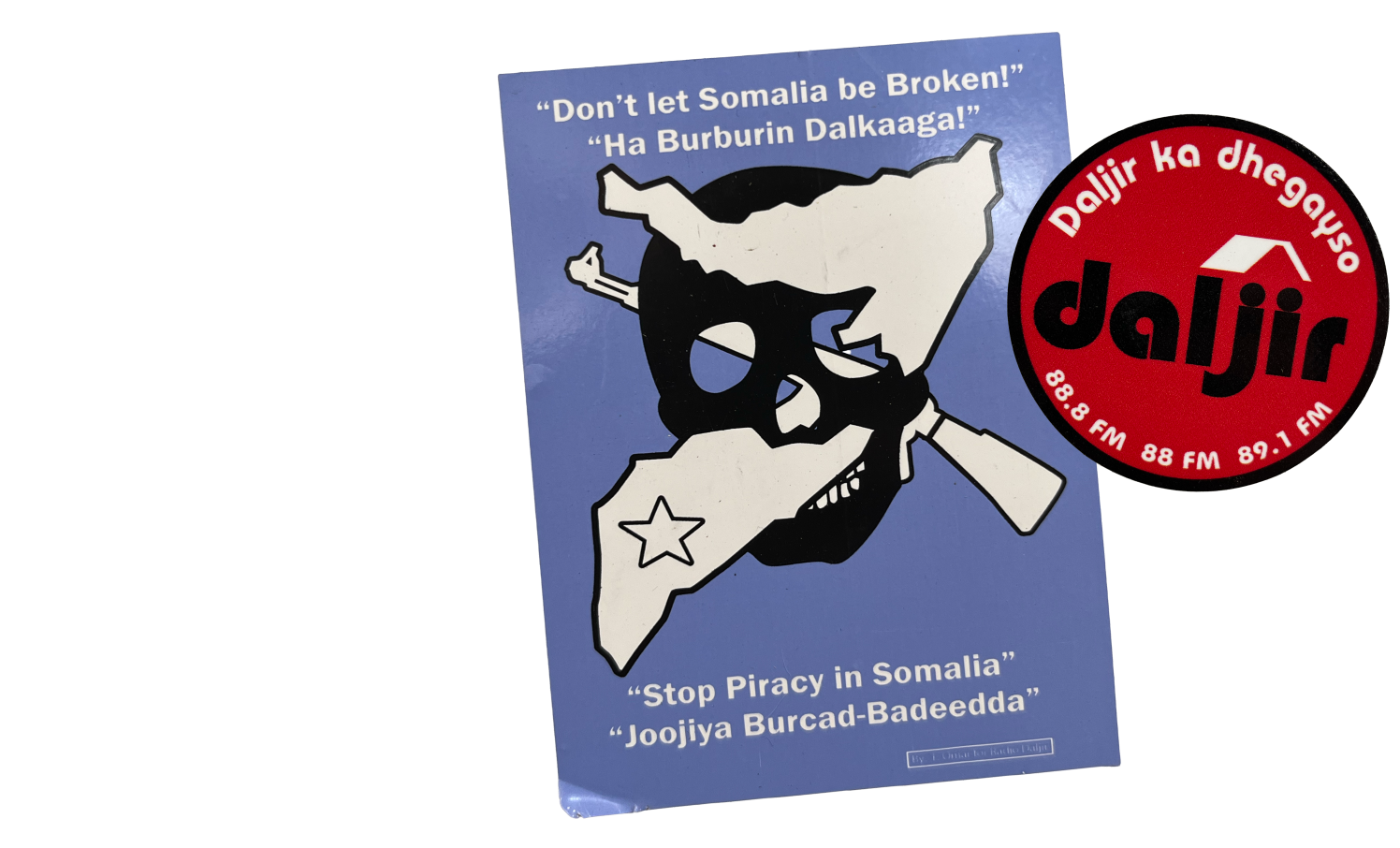 Two stickers are shown in a collage in the right column. One sticker is a rectangle with a light blue background. It has a black skull clip art with a white silhouette of a gun and the boundaries of Somalia crossing through the sockets of the skull. At the top of the sticker in white text in english it reads, “Don’t let Somalia be Broken!” under this text is a translated version in Somali. At the footer of the sticker the white text reads, “Stop Piracy in Somalia” with a translated version beneath it. 

There is a watermark for One Earth Future in the bottom right corner.

The second sticker is a circle. It is red with a black  border. White text in somali borders the top of circle while a logo reading “daljir” in black is in the middle. White text with the radio FM code is on the bottom of the sticker. 

The left column of the graphic explains, “Stickers from 
One Earth Future’s campaign against piracy in Somalia.”